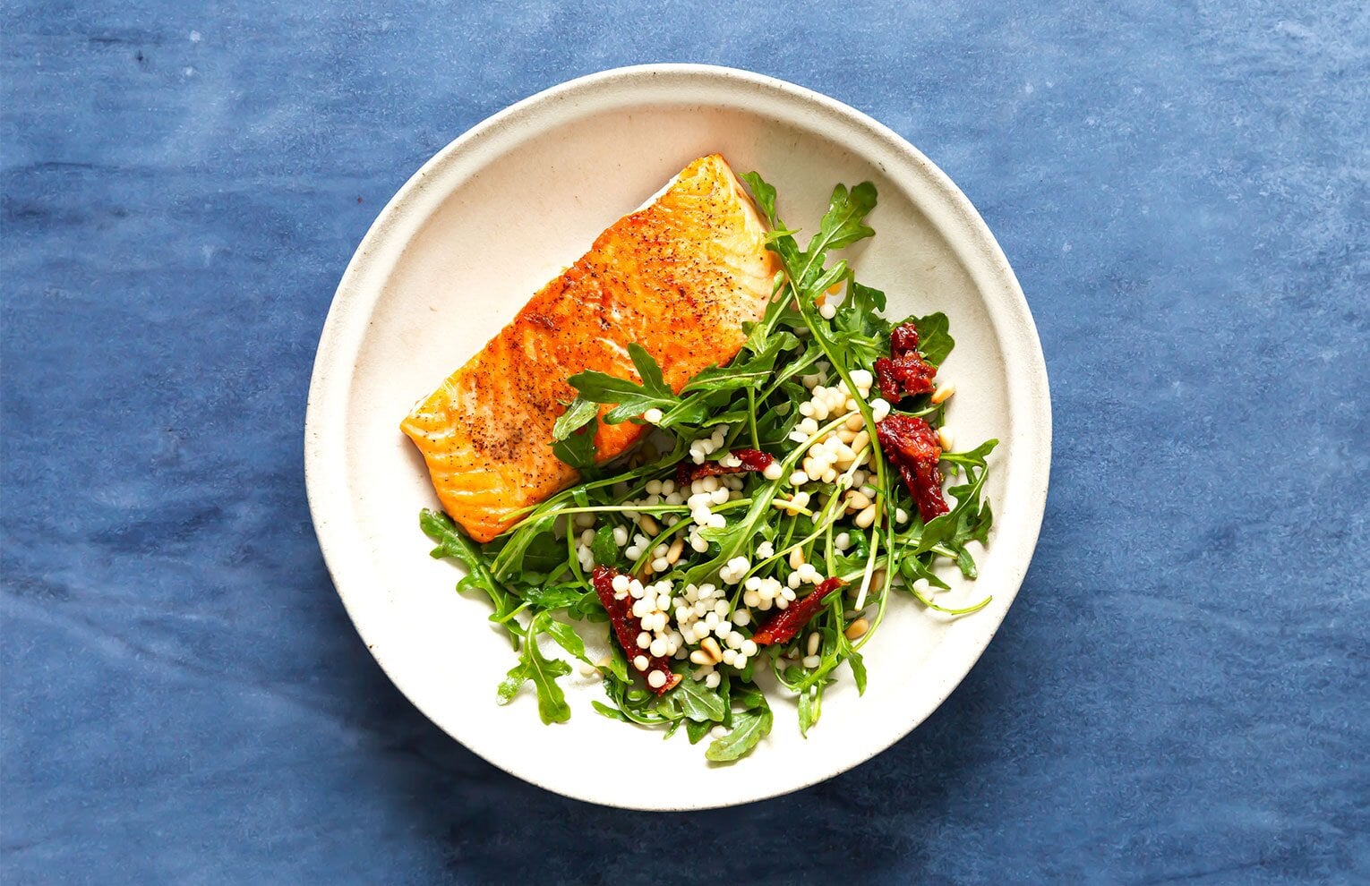 Arugula salmon salad with couscous, sun-dried tomatoes, pine nuts, and balsamic dressing 