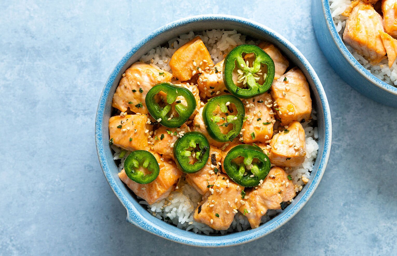 Two ramekins with salmon coated in a sriracha mayo sauce over rice. 