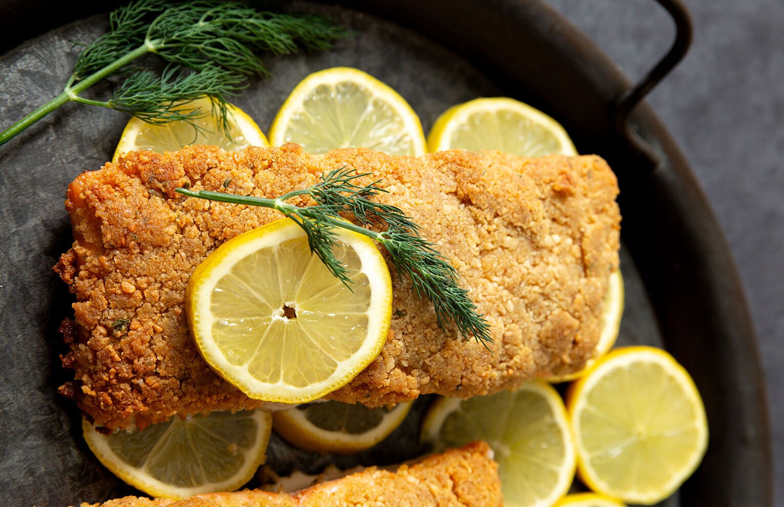 Salmon fillets topped with golden-brown breadcrumbs served with lemon wedges. 