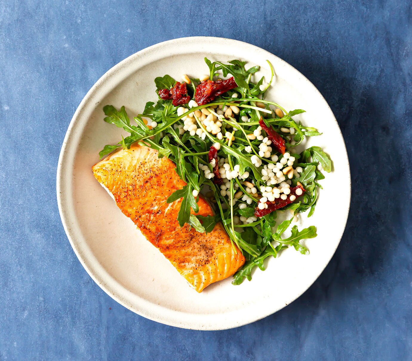 Arugula salmon salad with couscous, sun-dried tomatoes, pine nuts, and balsamic dressing 