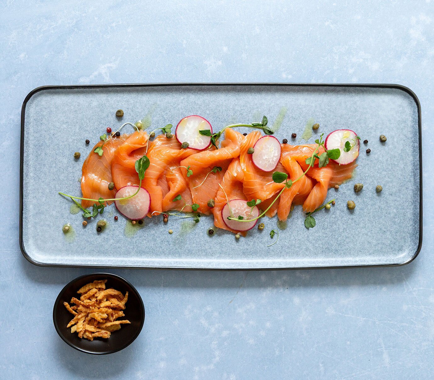 Salmon crudo served with capers, lemon juice, olive oil and topped with shaved radishes and crispy onions. 