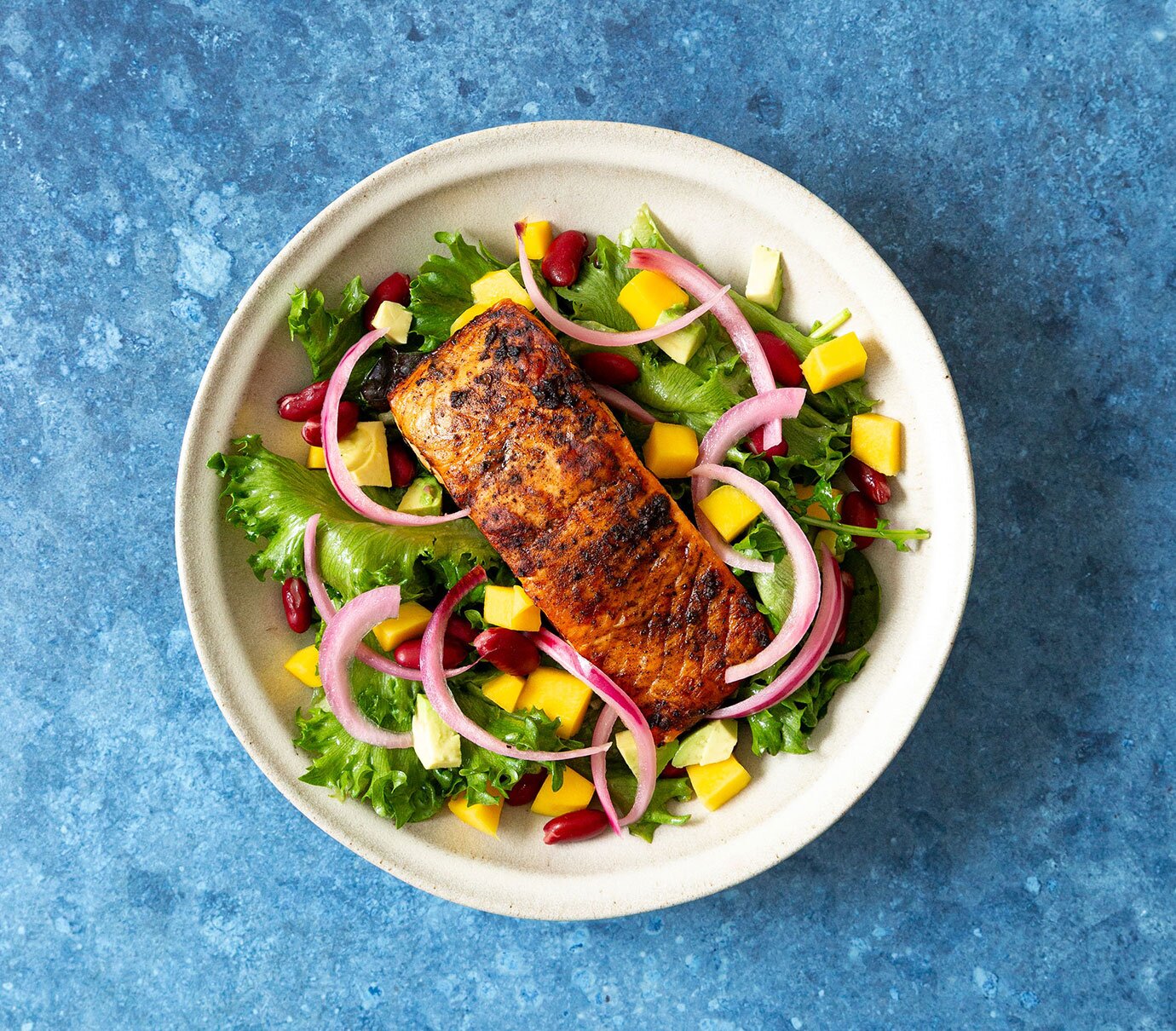 Pan-seared jerk salmon over mixed greens with pickled red onions, mango and avocado.  