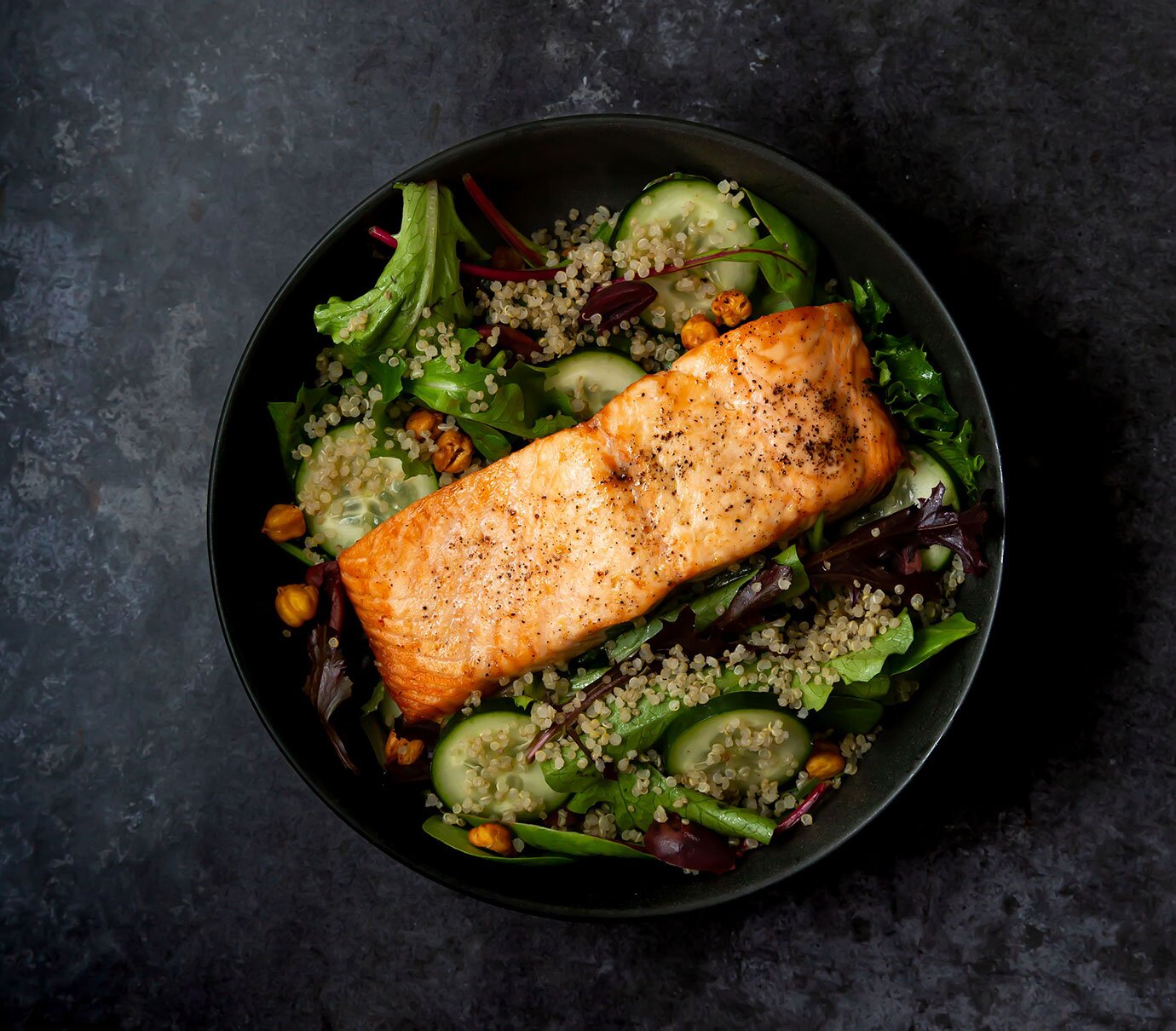Air-fried salmon served over baby lettuce with quinoa, cucumber, olives, and roasted chickpeas. 