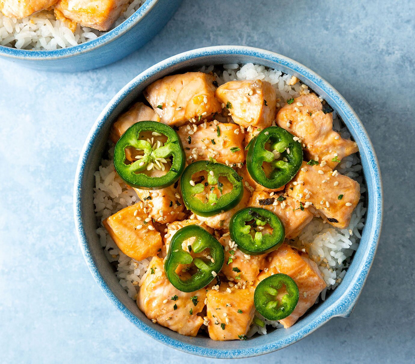 Two ramekins with salmon coated in a sriracha mayo sauce over rice. 